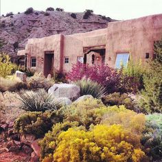 an adobe - style house surrounded by colorful plants and rocks in front of a mountain