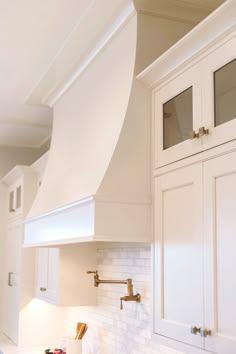 a kitchen with white cabinets and gold handles on the stove top, along with an oven hood