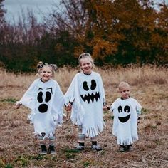 three children in halloween costumes holding hands and walking through a field with trees behind them