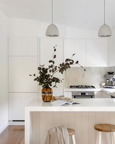 a white kitchen with two stools next to the counter and an island in front of it