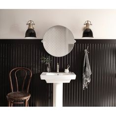 a white sink sitting under a bathroom mirror next to a wooden chair and wall mounted faucet