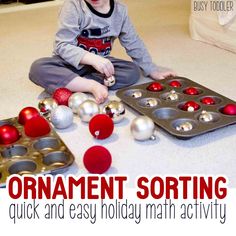 a young boy sitting on the floor playing with christmas ornaments and bake pans