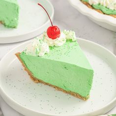 there is a slice of green cake on the plate and another piece has a cherry on top