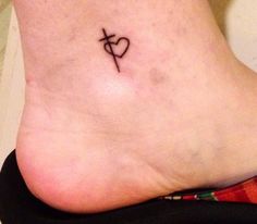 a small tattoo on the foot of a woman with a cross and heart in it