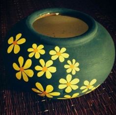 a vase with yellow flowers painted on it sitting on a wicker tableclothed surface