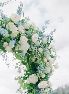 white and blue flowers are hanging from a pole with greenery in the foreground