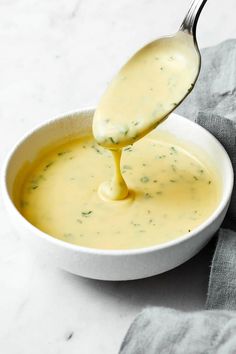 a white bowl filled with broth and being drizzled with a spoon