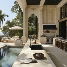 an outdoor kitchen and dining area next to a swimming pool in the middle of a house