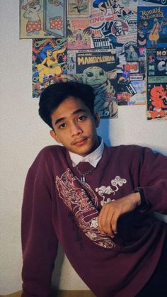 a man sitting on top of a wooden table next to a wall covered in posters