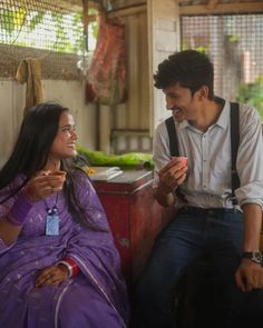 a man sitting next to a woman in a purple sari and smiling at each other