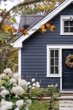 a blue house with a wreath on the front door and flowers in the foreground