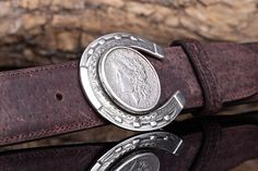 The Horseshoe & Morgan 1886 Trophy Buckle features a sterling silver horseshoe base with an embedded 1886 Morgan silver coin at its center. Measuring 2 7/8" x 2 3/8", this buckle is designed to fit all 1.5-inch belt straps. The moveable bale allows the belt to self-level, ensuring the buckle remains flat for a polished look. This unique piece combines historical significance with exceptional craftsmanship. Made in the USA. Classic Concho Belt Buckles For Formal Wear, Classic Formal Belt Buckles With Engraved Logo, Silver Western Belt Buckles For Formal Occasions, Formal Western Jewelry With Silver Buckle, Western Style Jewelry With Silver Buckle For Formal Occasions, Silver Coin, Silver Coins, Unique Pieces, Coin