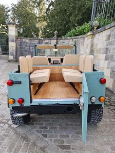 the back end of a truck with four seats on it's flatbed, parked in front of a stone wall