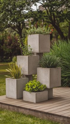 four cement planters with plants in them sitting on a wooden deck near grass and trees