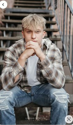 a young man sitting on top of a set of stairs with his hands under his chin