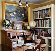 an old desk with books and globes on it in front of a bookcase