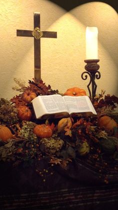 an open book sitting on top of a table next to a cross and pumpkins