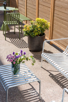 two chairs and a table with flowers in them on the ground next to a fence