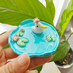 a hand holding a small toy duck in a pond with water lilies on it