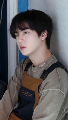 a young man wearing an apron leaning against a wall