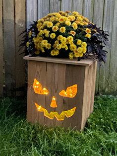 a wooden planter with yellow flowers in it and a jack - o'- lantern face painted on the side