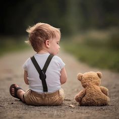 a little boy sitting on the ground next to a teddy bear and looking at something