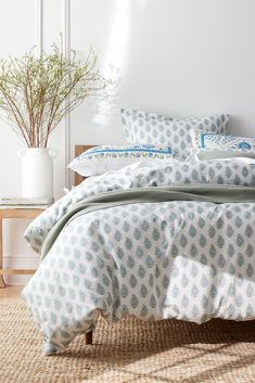 a bed with blue and white comforters in a room next to a plant on the floor