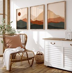 three paintings hang on the wall above a chair and sideboard in a white room