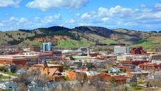 a city with mountains in the background and trees on the ground near buildings, grass and bushes