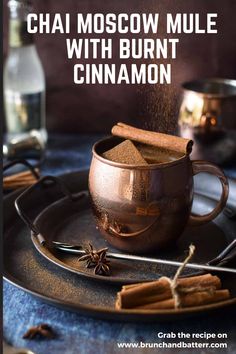 chai moscow mule with burnt cinnamon in a copper mug on a black plate, surrounded by cinnamon sticks and cloves