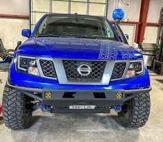 the front end of a blue truck in a garage with other cars and machinery behind it