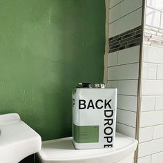 a white toilet sitting next to a green wall with a can on top of it