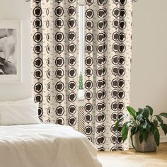 a white bed sitting under a window next to a plant in a room with wooden floors