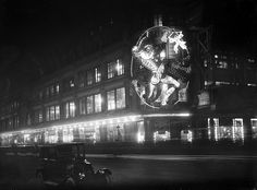 an old car driving down the street in front of a building with lights on it