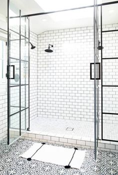 a bathroom with black and white tiles on the floor, glass shower doors, and tiled walls