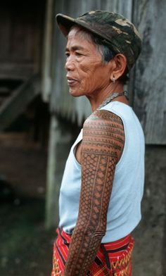 an old man with tattoos on his arm and chest standing in front of a building