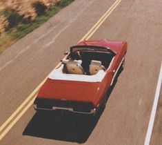 an old red convertible car driving down the road