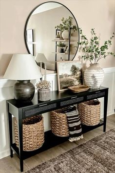 a black console table with baskets underneath it and a large round mirror on the wall