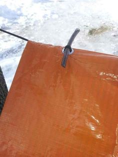 an orange tarp hanging from a tree next to the ocean with ice on it