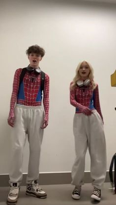 two people standing next to each other in front of a white wall wearing spiderman costumes