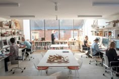 people sitting at desks in an office with bookshelves on the wall and open windows