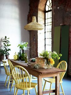 a wooden table topped with yellow chairs next to a tall planter filled with flowers