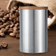 a stainless steel coffee canister next to some coffee beans on a wooden table with a burlap bag in the background