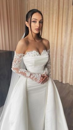 a woman in a white wedding dress with long sleeves and an off the shoulder veil