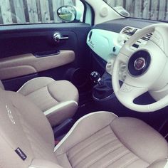 the interior of a small car with beige leather seats and steering wheel, in front of a wooden fence