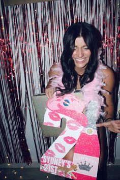 a woman holding up a cardboard number 2 sign with pink and silver decorations on it