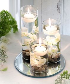 three candles are sitting in glass vases with rocks and flowers