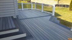 a wooden deck with white railings and gray siding on the side of a house