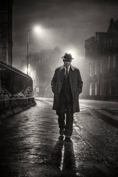 a man in a suit and tie walking down a street at night with an umbrella