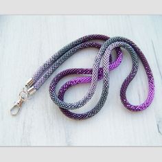 a purple and black dog leash on a white wooden surface with a silver metal hook